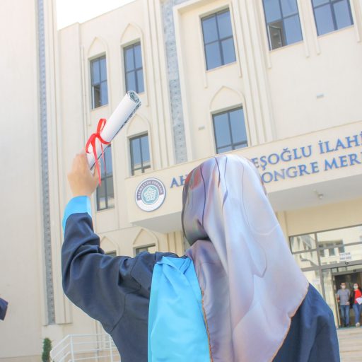 A graduate celebrates in front of a university holding a diploma.